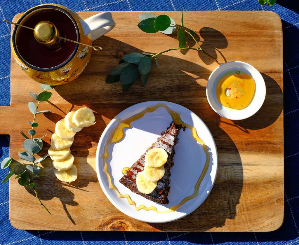 banaan-walnotentaartje van boven gefotografeerd. Geserveerd op een houten plank met thee en losse honing en banaan