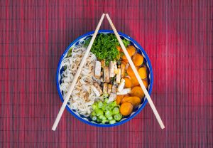 Schaal noedels met tofu en verse groente geserveerd op een bamboe placemat