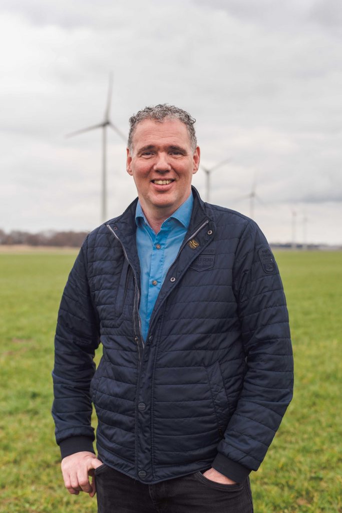 Ondernemer Hennie staat in een weiland vol windmolens