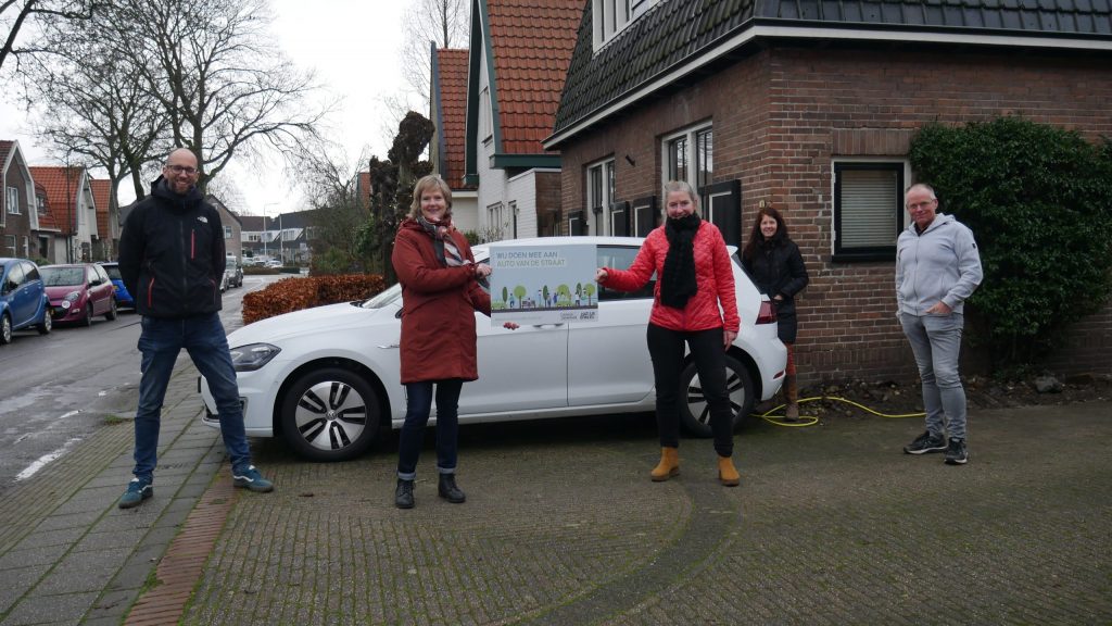Bewoners poseren voor een witte personenauto met een deelauto-deelname-bord