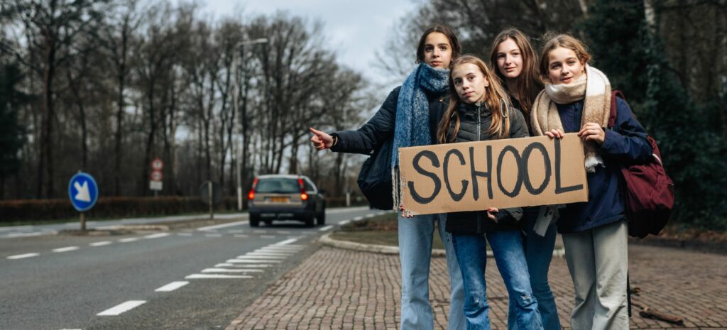 vier jonge scholieren staan langs de weg te liften naar school