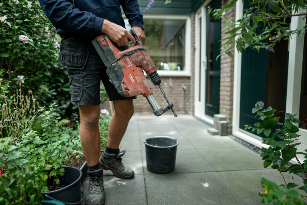 man staat met boormachine klaar in de tuin