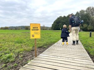 Foto van man met kind in natuurgebied, naast bord met 'Dit natuurgebied buiten gebruik? Dat moeten we voorkomen'