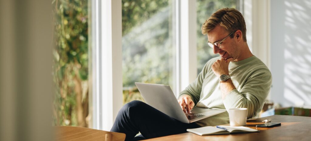 Man zit in de woonkamer en leest een nieuwsbrief op zijn laptop