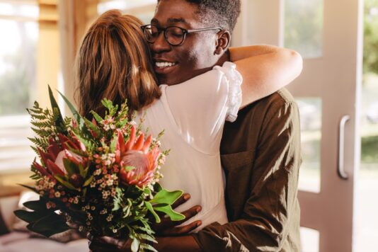 Man en vrouw in omhelzing, bos bloemen in de hand