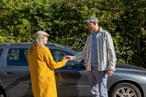 Vrouw geeft autosleutels aan man, bij een grijze auto