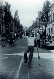 Zwart-witfoto uit de jaren zeventig van een lachend meisje dat speelt op straat in Nijmegen. Ze houdt twee stokken omhoog en staat midden op het asfalt, waarop met krijt is getekend.