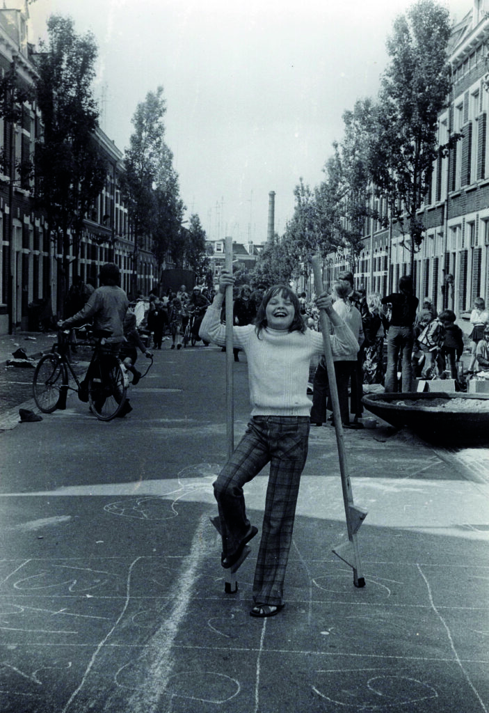 Zwart-witfoto uit de jaren zeventig van een lachend meisje dat speelt op straat in Nijmegen. Ze houdt twee stokken omhoog en staat midden op het asfalt, waarop met krijt is getekend.