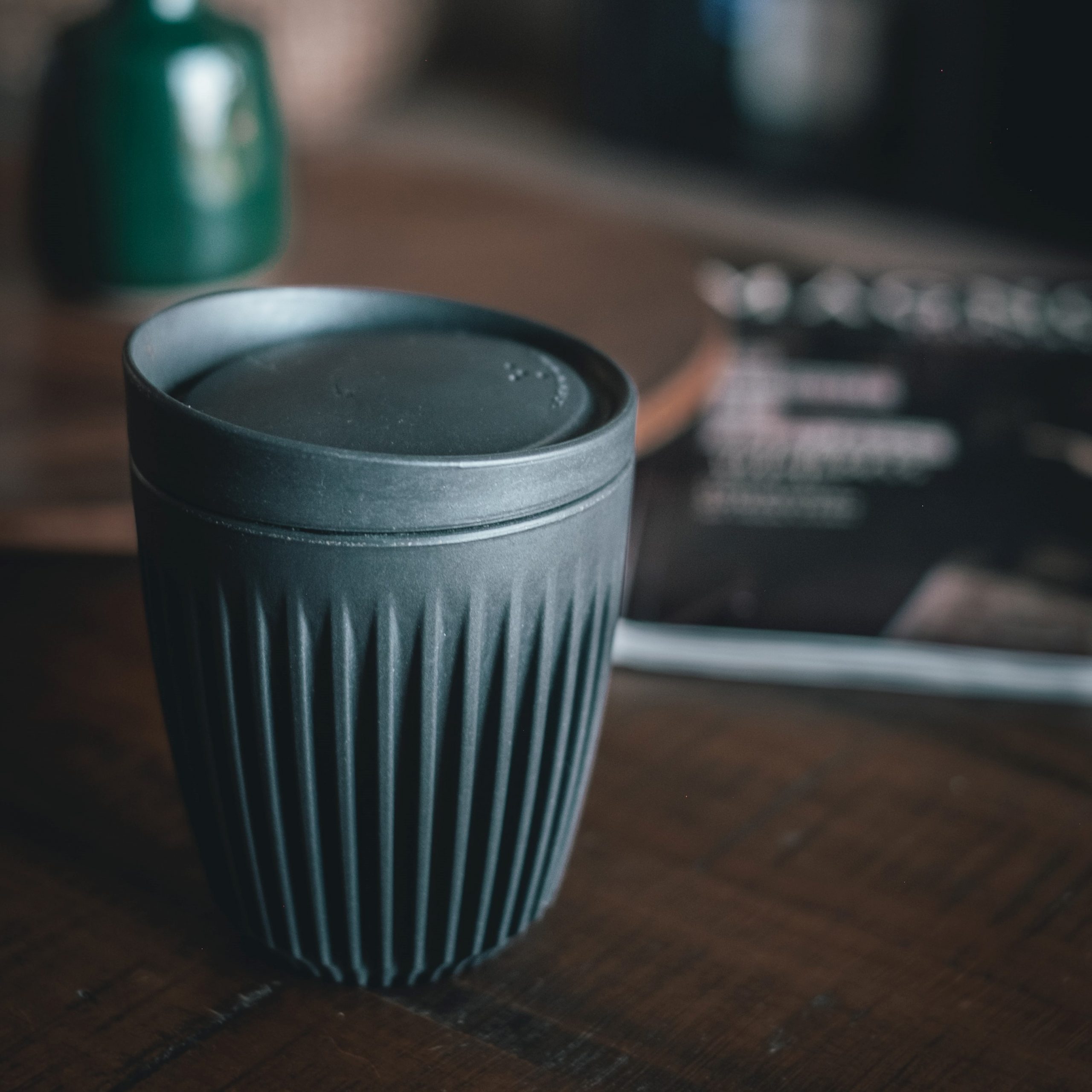 Een zwarte herbruikbare koffiebeker met deksel op een bruine tafel
