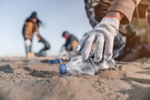 persoon pakt met handschoenen plastic flesje van het strand