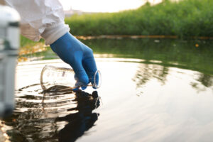 wateronderzoek: afvalwatermonsters uit industriële kanalen in een reageerbuis; close-up van een gehandschoende hand die monsters neemt