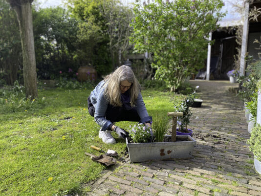 Vrouw zit gehurkt in tuin en vult een plantenbak