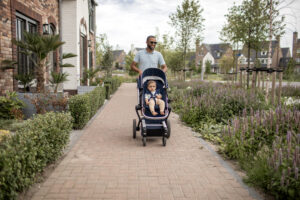 Vader met kinderwagen door groene buurt