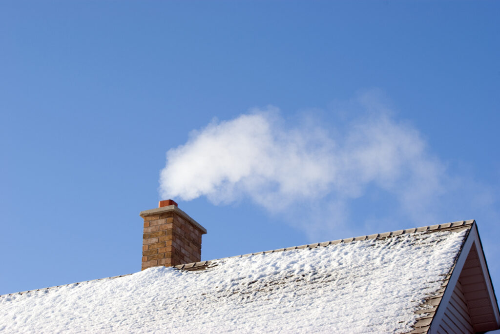 Rook uit schoorsteen op besneeuwd dak tegen heldere blauwe winterlucht