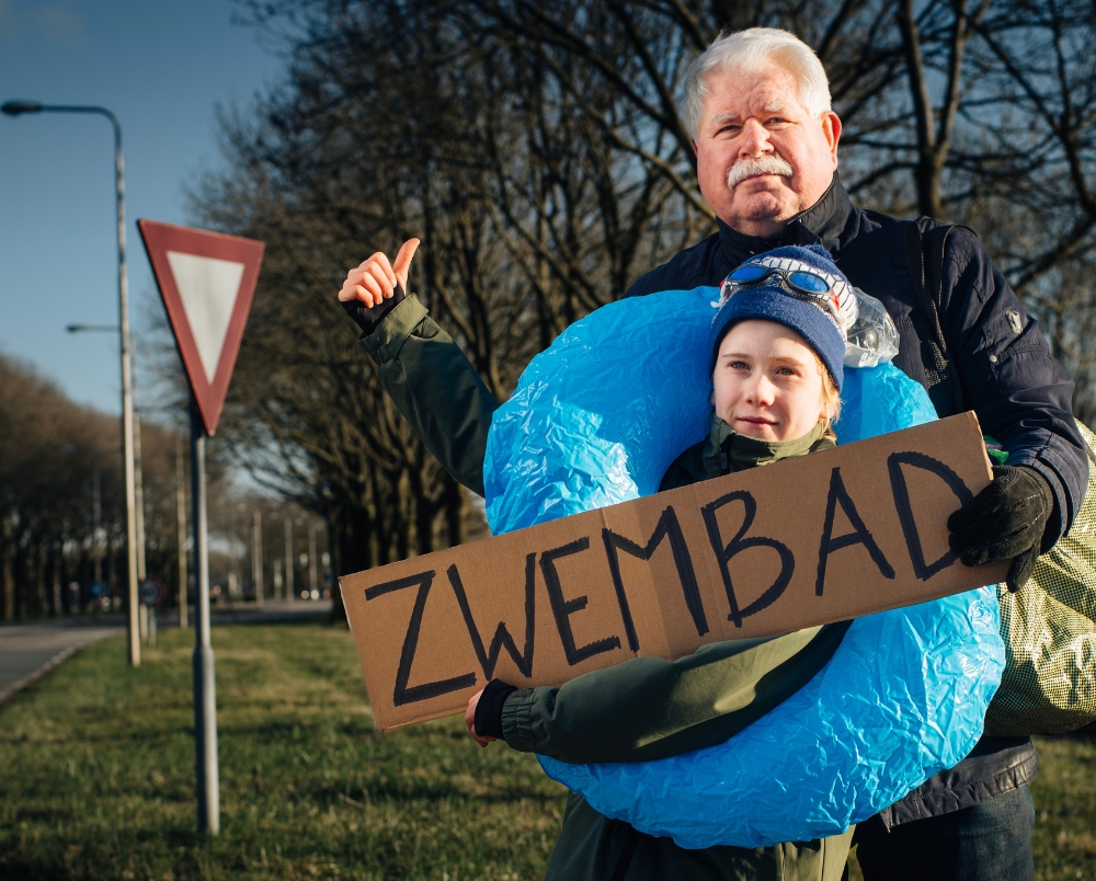 man en kind staan bij weg te liften met een bord met de tekst zwembad