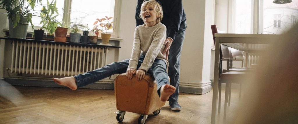Een kind wordt op een bokje rondgereden door opa in een woonkamer