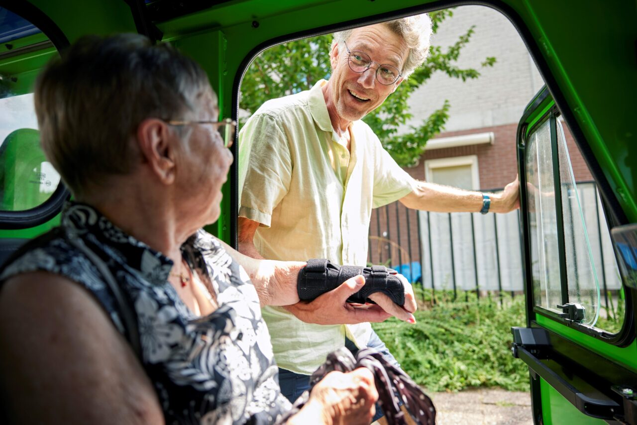 Man helpt een oudere vrouw om uit de auto te stappen