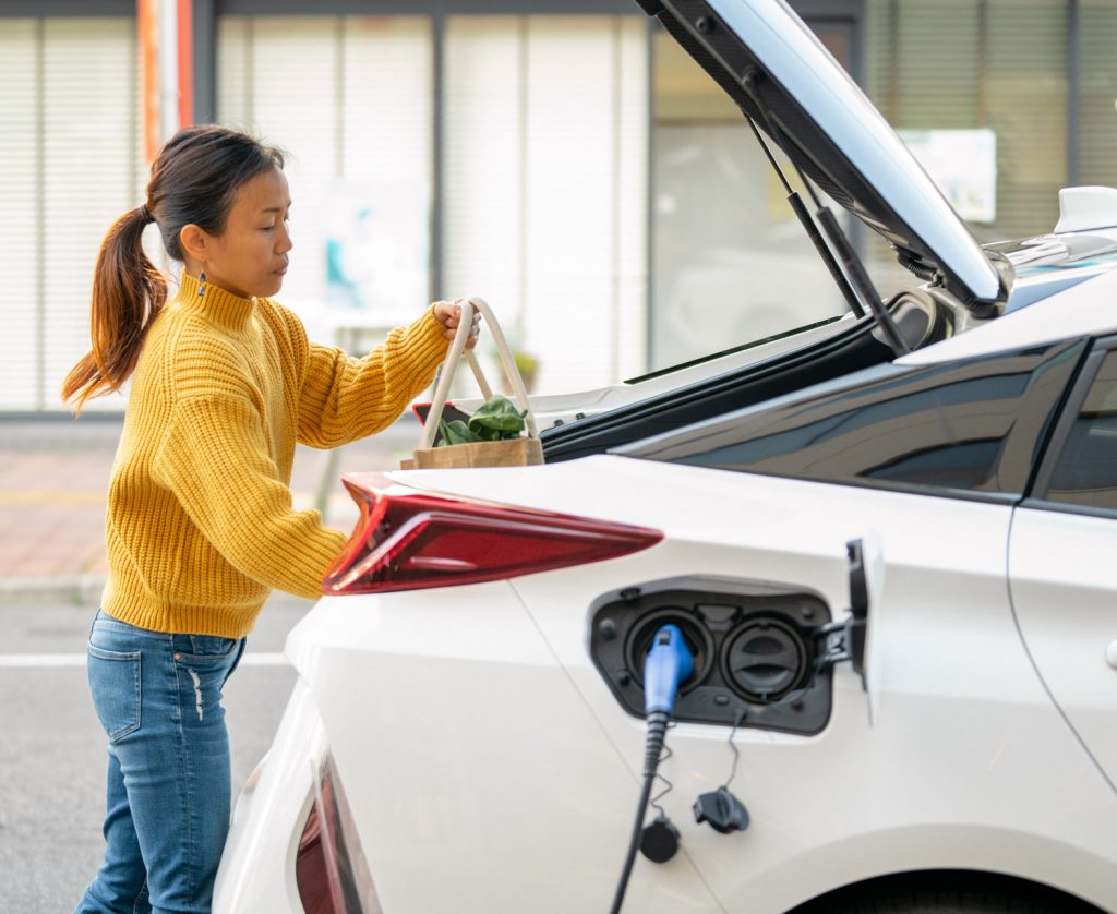 Vrouw stopt haar boodschappen in de achterbak van haar elektrische auto die aan het laden is