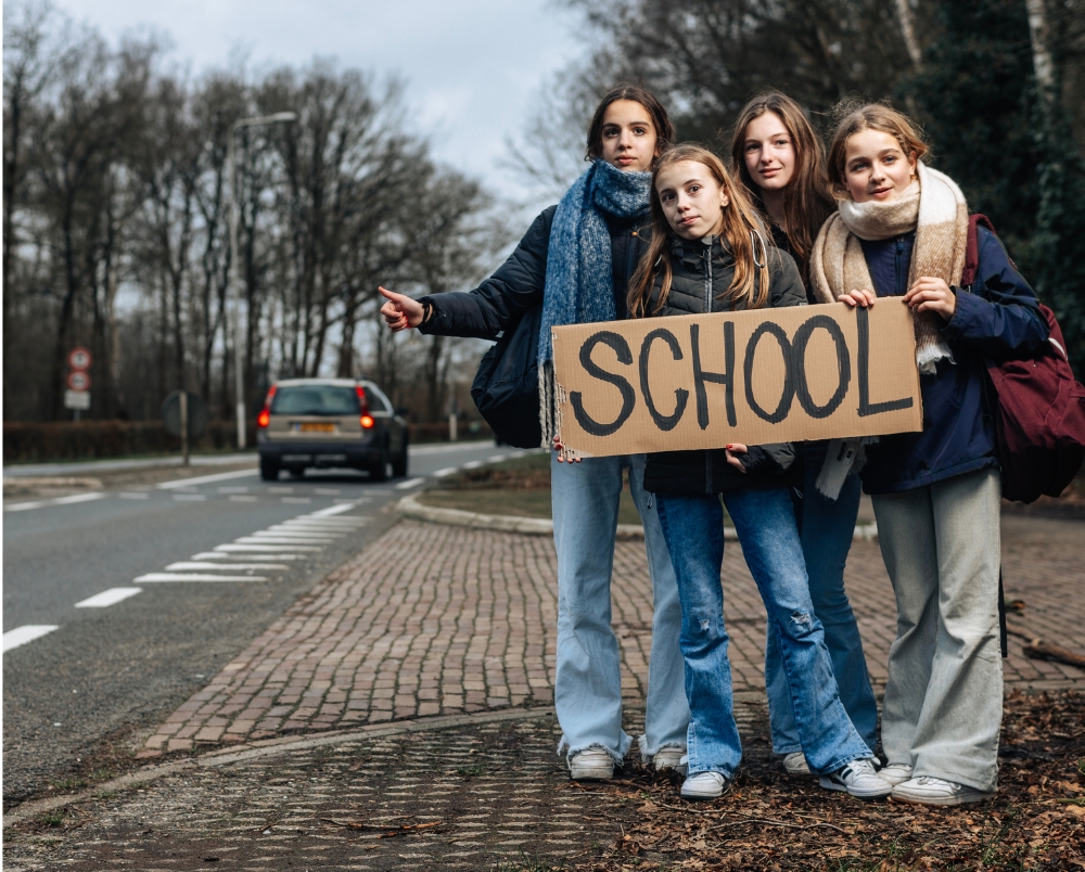 vier scholieren staan bij weg te liften met een bord met de tekst school